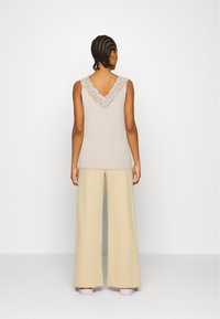 Débardeur beige clair avec un bord en dentelle en forme de V au niveau du col, porté avec un pantalon beige à jambes larges et des chaussures roses.