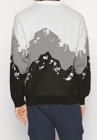 Maglione lavorato a maglia con un motivo montano in grigio, nero e bianco. Vestibilità ampia con polsini e orlo a coste, realizzato in tessuto traspirante.