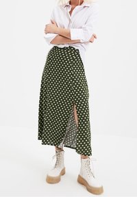 Green polka dot midi skirt with a side slit, made of lightweight fabric. Paired with white button-up shirt and beige lace-up platform boots.