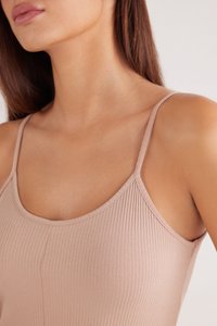 Camiseta sin mangas de color rosa claro con un diseño ajustado y tirantes finos, que presenta una textura suave y un sutil brillo en la tela.