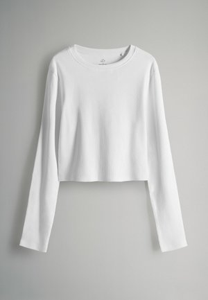 Biały, długi rękaw, krótki top wykonany z materiału ribbed z okrągłym dekoltem. Gładka faktura i brak widocznych wzorów czy akcentów.