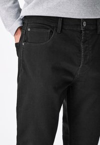 Blugi din denim negri au un design slim fit, cu un stil cu cinci buzunare, cusături contrastante și un închizător cu nasture la talie.