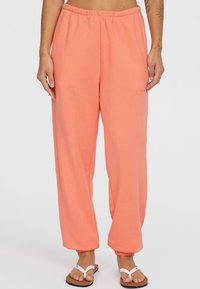 Perzikkleurige sweatpants van zacht materiaal, met een elastische tailleband en taps toelopende boorden. Subtiele logo-detail aan de voorkant.