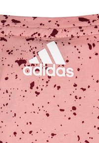 Rosa tyg med ett fläckigt mönster i mörkare nyanser. Har en vit Adidas-logotyp som är klart synlig.