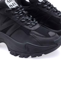 Sneaker atletici neri con tomaia in rete e materiali sintetici, suola testurizzata e lacci bianchi a contrasto. Presentano una punta arrotondata e collo imbottito.