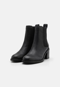 Bottines noires avec une tige en cuir lisse, des panneaux latéraux élastiques et un talon bloc. Elles présentent un bout arrondi et une languette à l'arrière.