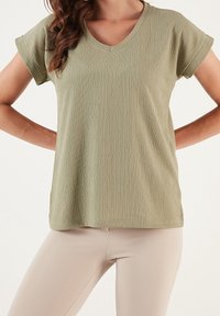 T-shirt verde oliva a scollatura a V realizzato in tessuto testurizzato; maniche corte, vestibilità rilassata, con orlo liscio e senza hardware visibili o dettagli.