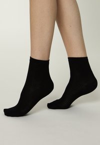 Schwarze Baumwoll-Sneakersocken mit geripptem Muster, einfarbigem Design und einer Schafthöhe bis zur Mitte der Wade. Glatter, dehnbarer Stoff.