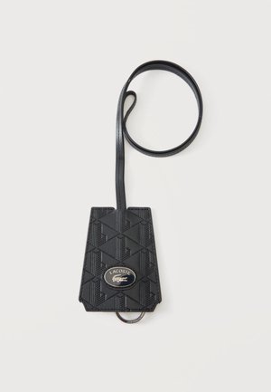 Funda para llaves Lacoste negra con patrón geométrico, correa larga, placa metálica con el logotipo y anilla metálica en la parte inferior, sobre fondo blanco.