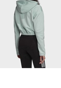 Kort grön hoodie med dragsnodd och elastisk midja, ihop med svarta leggings med vita ränder längs sidan.