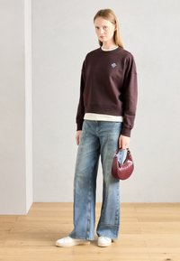 Sudadera burdeos con un pequeño logo, camiseta de capas de color claro, jeans azul claro de pierna ancha y un bolso burdeos texturizado.