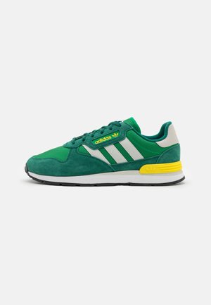 Green suede sneaker with white and silver accents, featuring yellow branding and a rubber sole. Classic athletic design with laces.