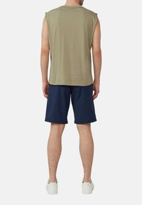 Un t-shirt sans manches vert olive associé à un short bleu marine. Le t-shirt a un col rond et une coupe décontractée ; des baskets blanches complètent le look.