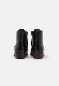 Bottes courtes en cuir noir avec une finition lisse, fermetures éclair latérales et un talon en bois, présentant des lignes épurées et un design minimaliste.