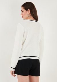 Weißer gestrickter Pullover mit einem gerippten schwarzen Streifen am Saum und an den Ärmeln, mit rundem Ausschnitt und langen Ärmeln.