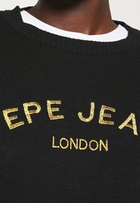 Maglione in maglia a costine nero con lettere dorate ricamate e testurizzate "PEPE JEANS LONDON" sul davanti. Strato bianco a girocollo visibile sotto.