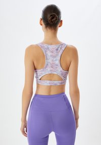 Lilla og lyserød tie-dye sports-bh med racerback-design og udskæringsdetalje. Blødt, strækbart stof i kombination med matchende lilla leggings.