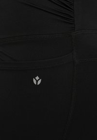 Zwarte leggings van rekbaar materiaal, met een gerimpeld ontwerp, platte naden en een klein grijs logo nabij de tailleband.