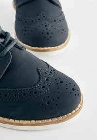 Chaussures en cuir gris foncé avec des détails perforés, bout arrondi et semelle claire contrastante. Présente un design classique avec lacets et des accents de couture.