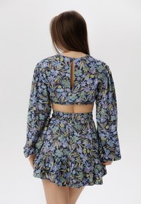 Set a due pezzi floreale in blu, composto da un crop top con maniche lunghe e apertura a chiave sul retro, e una mini gonna voluminosa con una vita elastica.