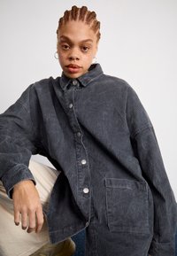 Šedá kordurová košeľa s kabátovým strihom, s gombíkovou prednou časťou, golierom a bočnou vreckou. Obsahuje vertikálnu ribovanú textúru pre dodatočný detail.