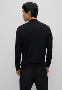 Fekete kötött pulóver kerek nyakkivágással és hosszú ujjakkal. Slim fit szabású, bordás mandzsettákkal és aljjával, puha, könnyű anyagból készült.