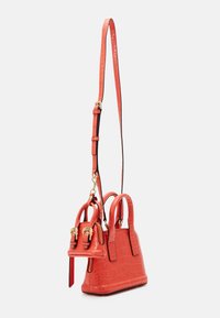Malá texturovaná červená kabelka s dvěma horními uchy a odnímatelným nastavitelným popruhem přes rameno, která má odpovídající mini taštičku jako přívěsek.