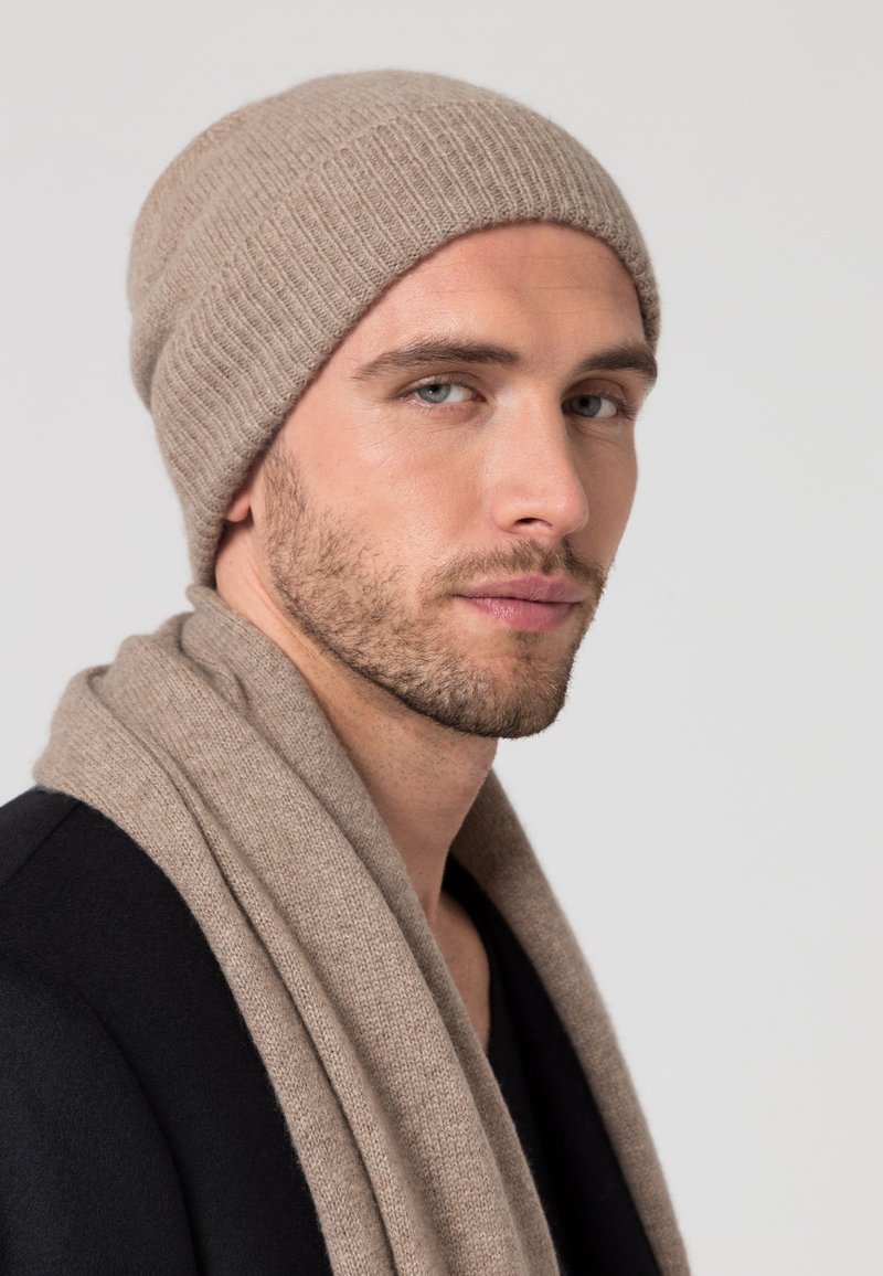Bonnet en tricot beige avec une texture côtelée, accompagné d'une écharpe assortie. Les deux sont fabriqués dans des matériaux doux et chauds. Design simple sans motifs.