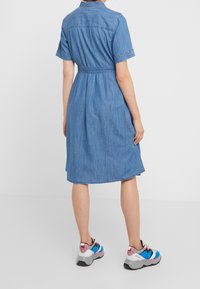 Džínové šaty s krátkým rukávem, s úzkým pasem, světle modrou látkou, rovním spodním lemem a detaily na zadním díle, doplněné barevnými sportovními botami.