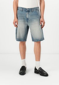 Shorts in denim con una finitura blu sbiadita, alla lunghezza del ginocchio, con tasche frontali e un leggero orlo sfrangiato. Abbinati a mocassini neri e calze bianche.