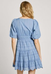 Jasnoniebieska bawełniana sukienka z bufiastymi rękawami, marszczonym stanem, warstwową spódnicą i zdobieniem broderie anglaise. Falowany dół sukienki.