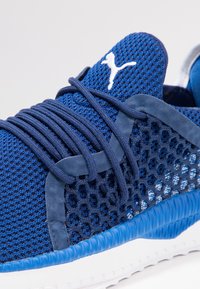 Niebieski sportowy but z siateczki z wiązaniem na sznurówki, wyściełanym kołnierzem, teksturowaną środkową podeszwą oraz białym akcentem w postaci logo.