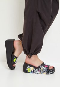 Saboti negri, tip slip-on, cu talpă groasă, având modele și accente colorate de graffiti. Fabricați dintr-un material durabil, cu un finisaj texturat.