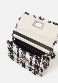 Schwarz-weiße Hahnentrittmuster-Tasche aus strukturiertem Stoff. Verfügt über einen silbernen Verschluss, ein beigefarbenes Innenfutter und einen schwarzen Lederriemen.