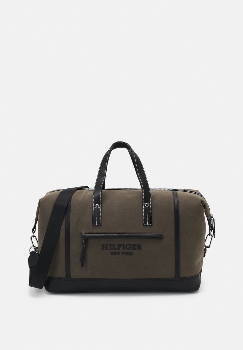 Sac de sport en toile vert olive avec des accents noirs, poignées supérieures et bandoulière réglable. Poche zippée à l'avant avec logo.