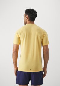 Camiseta amarilla de manga corta con una textura suave y un diseño ajustado, que presenta un cuello redondo y mangas raglán. Se combina con pantalones cortos de color navy.