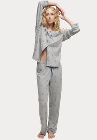 Grå pyjamasset bestående av en skjorta med knappar, blå kant och korta ärmar, som är kombinerad med byxor med elastisk midja, prydda med små blåa rosettmönster.