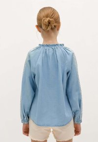 Himmelblaues Denim-Hemd mit langen Ärmeln, gesammeltem Ausschnitt und dreieckigen Musterdetails an den Schultern. Glatte Textur und lässige Passform.