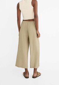Pantalons larges en khaki avec un tissu texturé et une taille élastique, associés à un haut ajusté beige et des sandales plates.