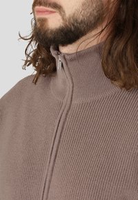 Pullover mit Viertelreißverschluss aus weichem, geripptem Strickstoff in helltaupe, mit hohem Kragen und silberner Reißverschluss-Ziehschlaufe.