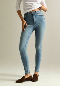 Högmidjade ljusblå skinny jeans i denim med en slät yta. Kombinerat med mörkbruna loafers med en strukturerad detalj.