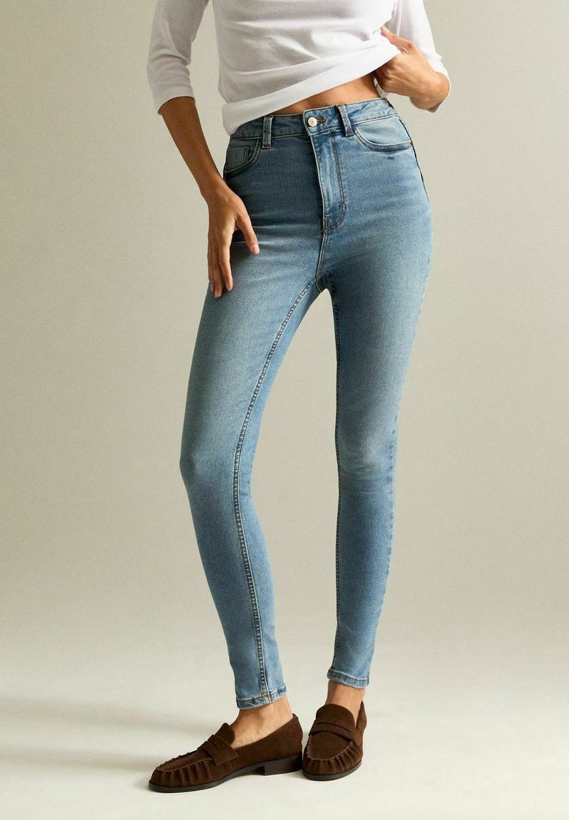 Högmidjade ljusblå skinny jeans i denim med en slät yta. Kombinerat med mörkbruna loafers med en strukturerad detalj.