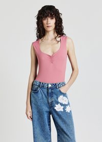 Body rosa senza maniche con scollo a barca e dettagli arricciati, abbinato a jeans azzurri a gamba larga con ricamo floreale bianco.