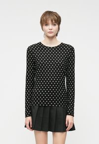 Svart langermet topp med hvite prikker. Rund hals, tettsittende design og ribbestrikket tekstur. Matchende med en svart plisserte skjørt.