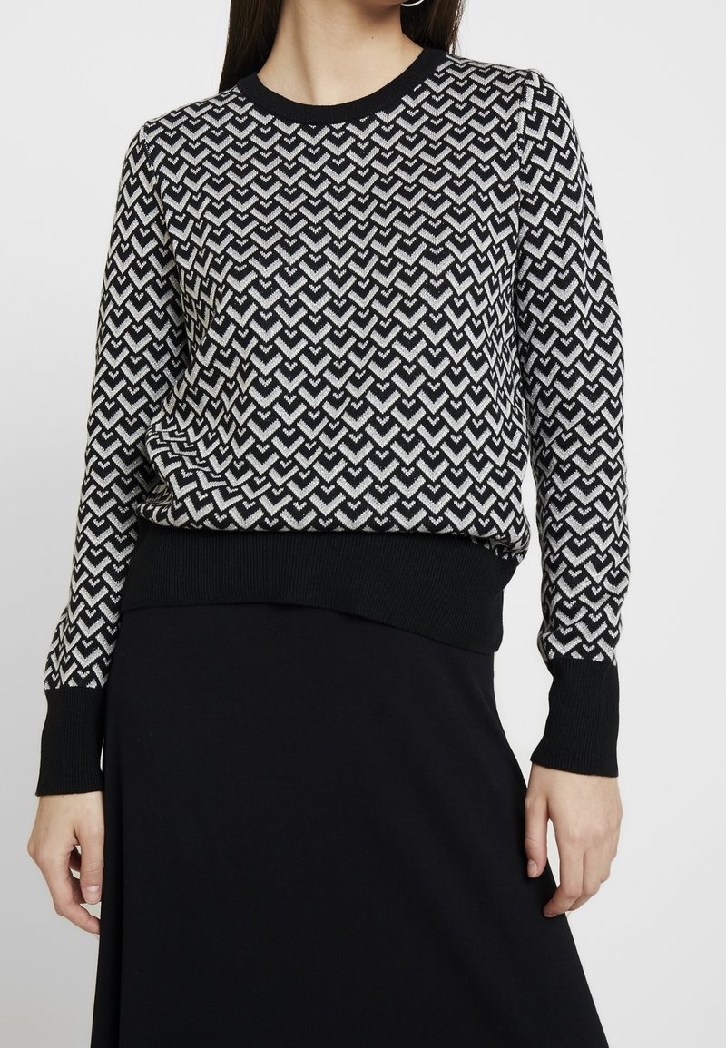 Maglione a righe in bianco e nero con design a zigzag, scollatura a girocollo e polsini e orlo a coste, realizzato in tessuto lavorato a maglia.