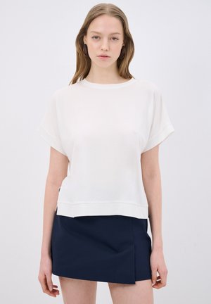 Top blanco de manga corta con un corte relajado, presenta un escote redondeado y un dobladillo acanalado, combinado con una falda mini de color azul marino.
