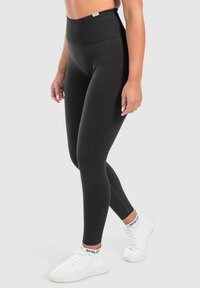 Hoge, zwarte leggings van rekbaar materiaal, met een gladde textuur en een enkel-lengte ontwerp, gecombineerd met witte sportschoenen.