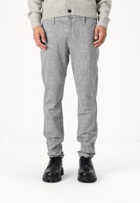Graue kariertef Hose aus leichtem Stoff, mit schmaler Passform, seitlichen Taschen und Knopfverschluss. Kombiniert mit schwarzen Schuhen.