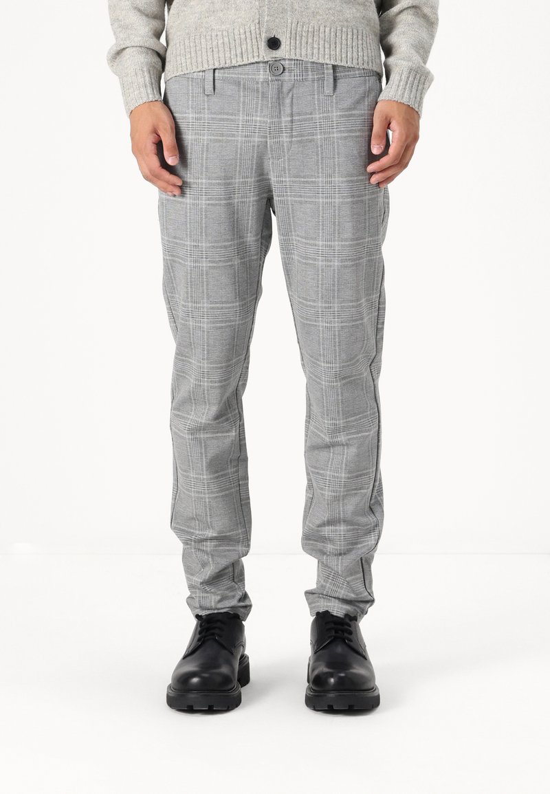 Graue kariertef Hose aus leichtem Stoff, mit schmaler Passform, seitlichen Taschen und Knopfverschluss. Kombiniert mit schwarzen Schuhen.