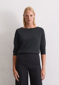 Zwart langemouwen shirt met een wijde halslijn en aansluitende mouwen, gemaakt van zachte stof. Gecombineerd met hoge taille zwarte broek.